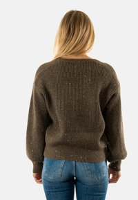 Maglione marrone, con una texture morbida e una vestibilità ampia, motivo a coste e riflessi metallici. Abbinato a jeans blu, che mostrano uno stile casual.