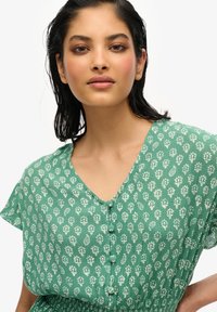 Vestido verde con estampado que cuenta con un escote en V, mangas cortas, detalles de botones y una tela texturada con motivos florales.