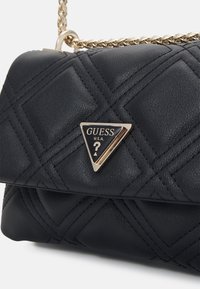 Zwarte gevoerde leren handtas met een gouden schakelkettinkje en een driehoekige logo-plaat met "GUESS U.S.A." aan de voorkant.