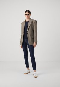 Přiléhavý béžový kockovaný blazer ve větší velikosti s jedním knoflíkem, kombinovaný s námořnickým topem, tmavými úzkými džíny a bílými teniskami s gumovou podrážkou.