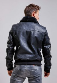 Veste bomber en cuir noir avec un col en fausse fourrure, des poignets et un ourlet côtelés, une texture lisse et une coupe ajustée. Portée avec un jean gris.