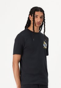 Black short-sleeve t-shirt made from cotton. Features a colored graphic design on the left chest and a crew neckline.