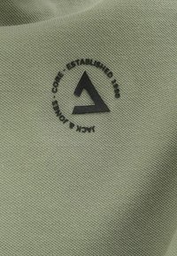 Zeleni pamuk s kružnim crnim logotipom koji sadrži natpis "CORE ESTABLISHED 1980" i trokutasti dizajn u središtu.
