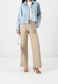 Ljusblå denimjacka med vita ränder, beige vida byxor, bandade klackar och en liten vit handväska.