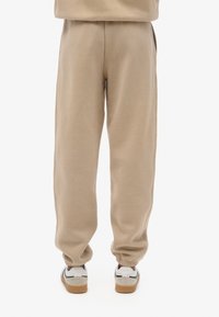 Pantalones de chándal beige con puños elásticos y bolsillos laterales, fabricados en material suave. Combinados con zapatillas blancas y grises con suela de goma.