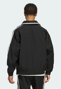 Schwarze Jacke mit weißen Streifen an den Schultern, mit lockerem Schnitt und elastischen Bündchen, aus leichtem Stoff gefertigt.