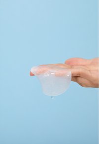 Transparent gel-lignende produkt hviler på en hånd, med en glat overflade og let glans, mod en blød blå baggrund.