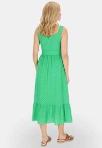 Zielona, sięgająca kolan sukienka z dopasowaną górą, rozkloszowanym dołem, w kropki, z falbaną na końcu, uszyta z lekkiego materiału.