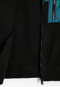 Czarna polarowa kurtka z kontrastowym panel na piersi w kolorze teal, z zapięciem na zamek z przodu i elastycznymi mankietami, o miękkiej fakturze na całej powierzchni.