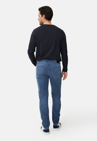 Dunkles Langarmshirt kombiniert mit hellblauen Jeans, zeichnet sich durch ein schlankes Design mit Gesäßtaschen und dezenten Steppnähten aus.