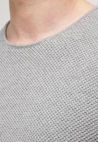 Grijze gebreide trui met een ronde halslijn, voorzien van een textuur patroon en zachte stof, close-up van de kraag en het bovenste gedeelte van de borst.