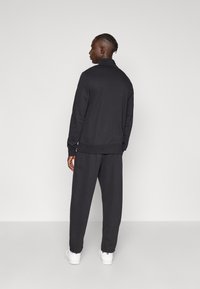 Ανδρική μαύρη φόρμα από λείο βαμβακερό μείγμα, με φερμουάρ και ψηλό γιακά, καθώς και ελαστικά μανσέτες, συνοδευόμενη από αντίστοιχο παντελόνι με άνετη εφαρμογή.