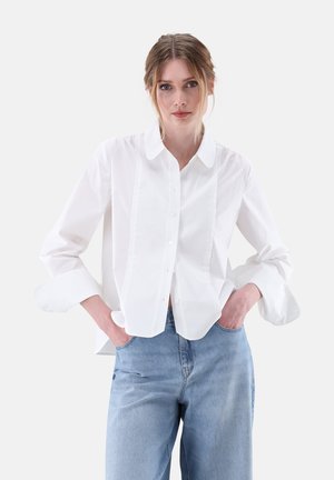 Weißes Hemd mit Knöpfen aus glattem Stoff, mit spitzem Kragen, seitlichen Nähten und umgeschlagenen 3/4-Ärmeln, kombiniert mit hellblauen Jeans.