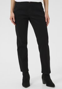 Jean taille haute noir avec poches latérales et détails cousus, associés à des bottines en suède noir et un haut blanc. Texture lisse.