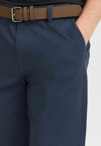 Pantalones azul marino con una textura suave, que cuentan con bolsillos laterales y un cinturón marrón con una hebilla plateada. Corte ajustado y tejido duradero.
