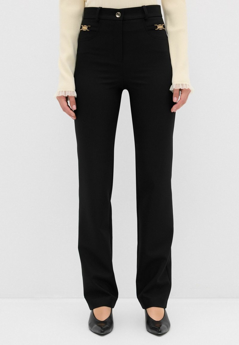 Pantalones negros ajustados con cintura alta, que presentan detalles metálicos dorados en los bolsillos y una tela suave y elástica.