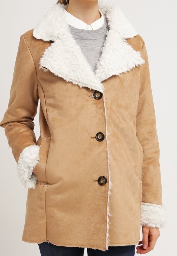 Beige faux suede kappa med en vit fuskpälskrage och manschetter. Har en enkelknäppt design, fem knappar och två sidofickor.