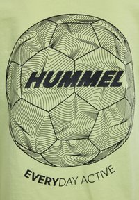 Lys limegrøn t-shirt med en sort omridset fodboldgrafik. "HUMMEL" og "EVERYDAY ACTIVE" teksten fremtrædende vist.