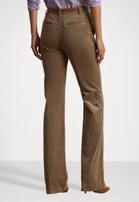 Pantaloni a palazzo in corduroy marrone con sottili righe verticali, due tasche posteriori e passanti per cintura, abbinati a una maglietta leggera viola infilata dentro.