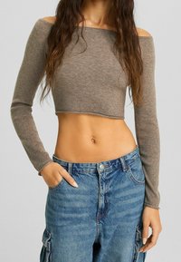 Top marrón acanalado, corto, con escote barco y mangas largas, combinado con jeans cargo de talle alto azules. Textura notable, buen ajuste y diseño casual.