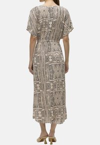 Maxime vestido em tecido bege claro com padrão geométrico preto, mangas curtas, cintura elástica e design fluido.