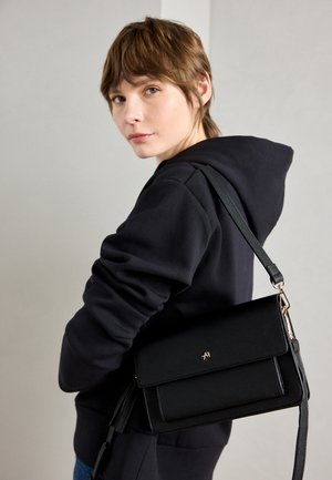 Zwarte leren crossbody tas met een omslagflap, gouden logo en verstelbare schouderband. Eenvoudig ontwerp met een gladde textuur en geen zichtbare patronen.