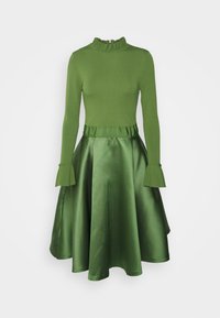 Vestido verde con mangas largas de punto, cuello y puños con volantes, acompañado de una falda acampanada de satén, de longitud media, expuesto sobre un fondo blanco.