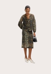 To-delt outfit med en gennemsigtig, mønstret bluse med voluminøse ærmer og en matchende nederdel i knælængde med lignende design. Hvide sko og en lille sort taske.