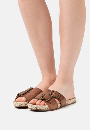 Brune slide sandaler har strukturerede læderstropper med to store spænder, en flettet jute sål og et åbent tå-design.