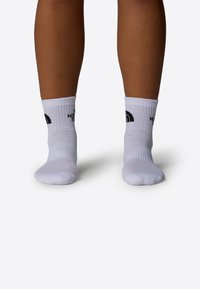 Calcetines blancos hasta el tobillo con puños acanalados. Presenta texto y gráfico de logo en negro en el lateral. Fabricados con una mezcla de materiales de algodón.