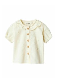 Blusa a maniche corte di colore crema con colletto arricciato, cinque bottoni in legno e pois testurizzati su un tessuto morbido.