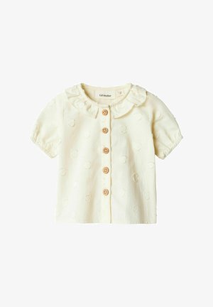 Blusa a maniche corte di colore crema con colletto arricciato, cinque bottoni in legno e pois testurizzati su un tessuto morbido.