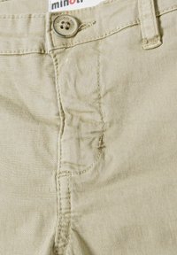 Pantalons en coton beige clair avec une texture lisse, dotés d'un bouton en métal, de détails cousus et d'une poche avant.