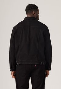 Mustast teksajope klassikalise lõikega, millel on sirge tagaosa, nööbitavad mansetid ja küljetaskud. Sujuv tekstuur, nähtavad mustrid puuduvad.