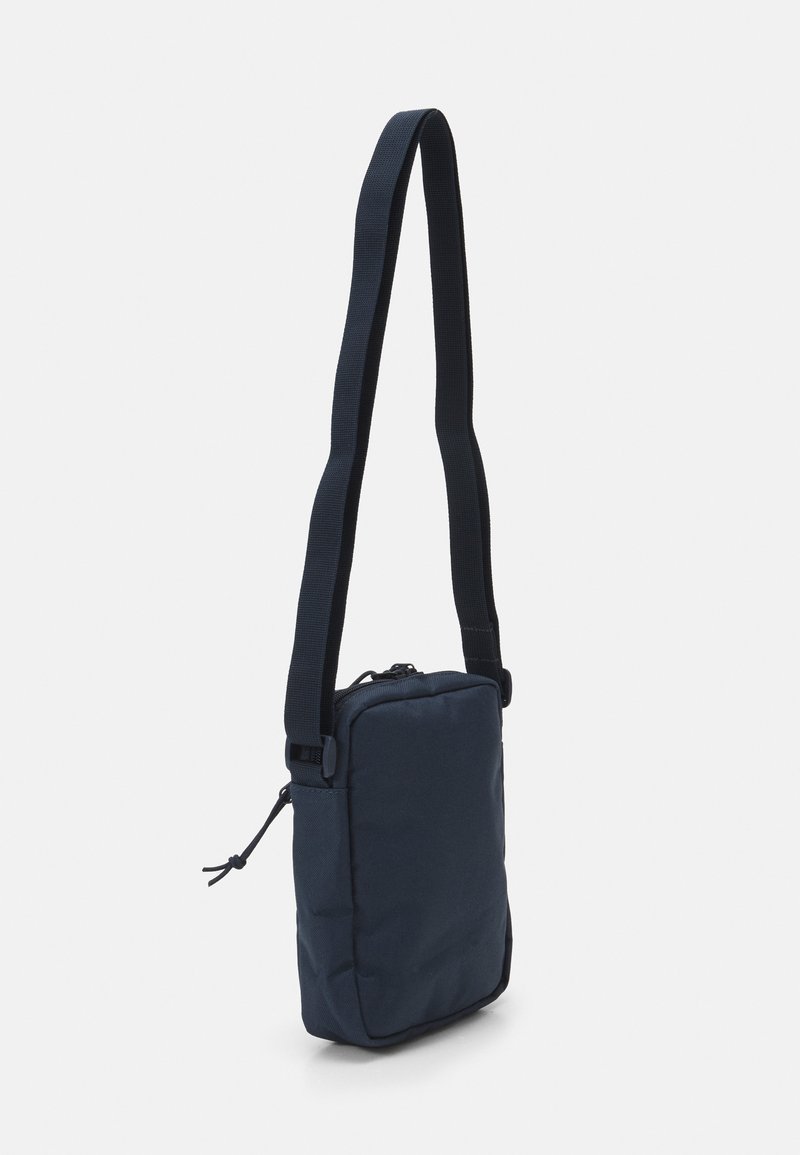 Sac bandoulière rectangulaire bleu marine en tissu texturé, avec une longue sangle réglable et une fermeture zippée sur le dessus.