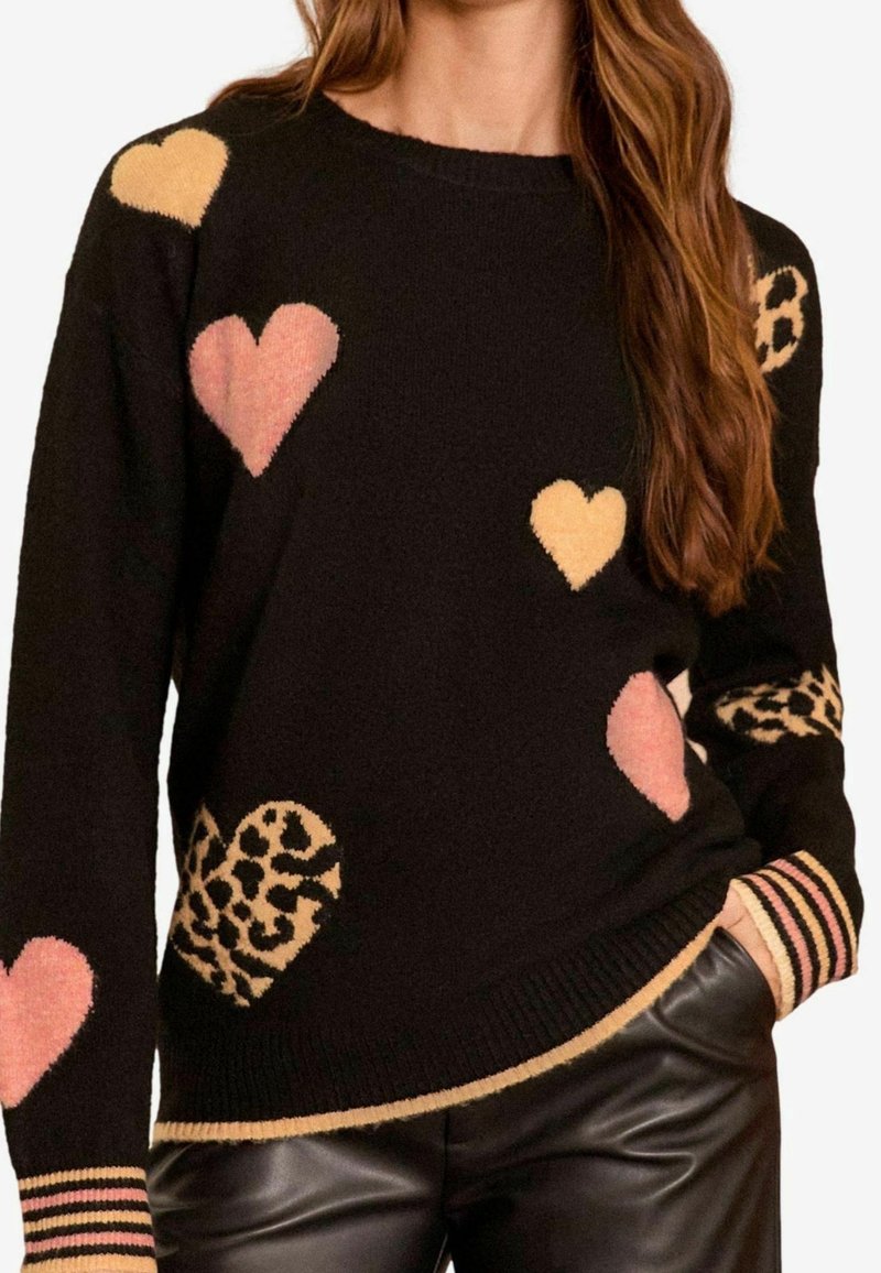 Maglione nero con fantasie di cuori rosa, gialli e leopardati, polsini a coste con righe, abbinato a pantaloni di pelle neri.