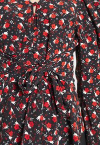 Robe portefeuille noire à fleurs avec des fleurs rouges et des accents blancs, dotée d'un col boutonné, de manches bouffantes et d'un détail de ceinture nouée.