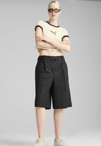 Beskarvet beige t-shirt med sort kant og farverig broderi, parret med sorte skræddersyede shorts og båret med lysegrå slip-on sko.