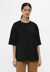 Black oversized t-shirt made of cotton, featuring a crew neck, short sleeves, and a relaxed fit. Paired with light brown pants.