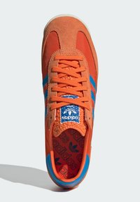 Oranje sneaker met een bovenwerk van suède en canvas, blauwe strepen, een gestructureerd blauw tonglabel en een met patronen bedrukt binnenzool. Bevat platte oranje veters.