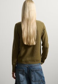 Pullover in maglia verde oliva con design aderente, polsini e orlo a coste. Indossato con pantaloni cargo in denim blu dotati di grandi tasche.