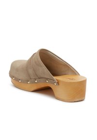 Beige suède klomp met een houten platform, een ronde neus en goudkleurige studs langs de basis, met een gestikte accent.