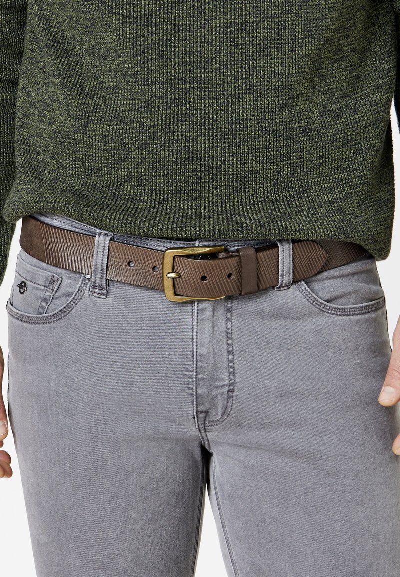 Braun gestreifter Gürtel mit einer Metallschnalle, getragen über grauen Jeans. Der Pullover ist dunkelgrün aus strukturiertem Strickstoff. Fokus auf der Taillenregion.