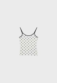 Camisole blanche sans manches avec fines bretelles noires et pois noirs dispersés sur un fond clair uni.
