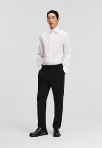 Witte button-down shirt met een gestructureerde kraag, gecombineerd met zwarte geplooide broek met een elastische tailleband en zwarte veterschoenen.