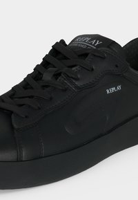 Baskets noires de la marque Replay avec lacets noirs, dessus en cuir lisse et semelle épaisse noire, présentées de profil sur un fond clair.