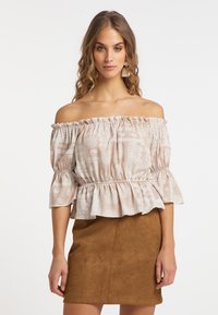Blusa off-the-shoulder in beige chiaro con motivi bianchi, maniche a volant e vita aderente abbinata a una gonna in suede marrone.