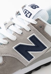 Férfi New Balance 574 sneaker szürke velúrból és kék hálóból. Fehér fűzőkkel, navy logóval és textúrázott díszítésekkel a felső részen. Fekete talp.