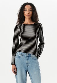 Svart og beige stripete langermet skjorte med rund hals, sammen med lyseblå høyt liv jeans. Jevn tekstur.