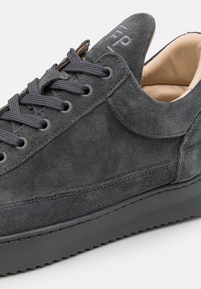 Harmaa mokkanahkainen sneaker, jossa on musta kumipohja, pyöreät nauhat ja kohokuvioitu logo. Varustettu pyöreällä kärjellä ja sileällä sisävuorella.